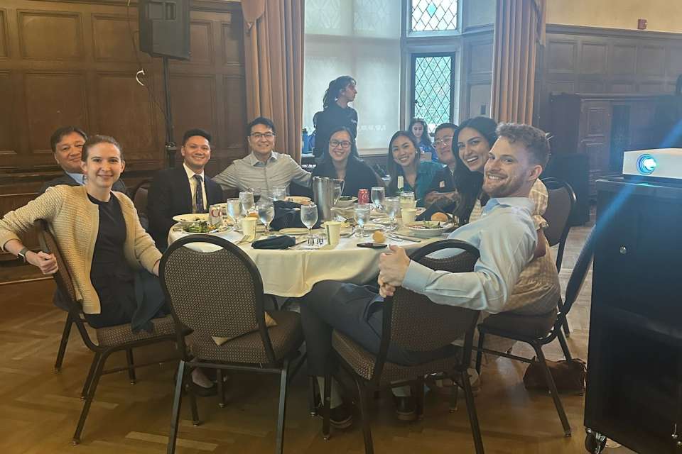  A group of people are seated around a round table with a white tablecloth in a formal room, smiling towards the camera.