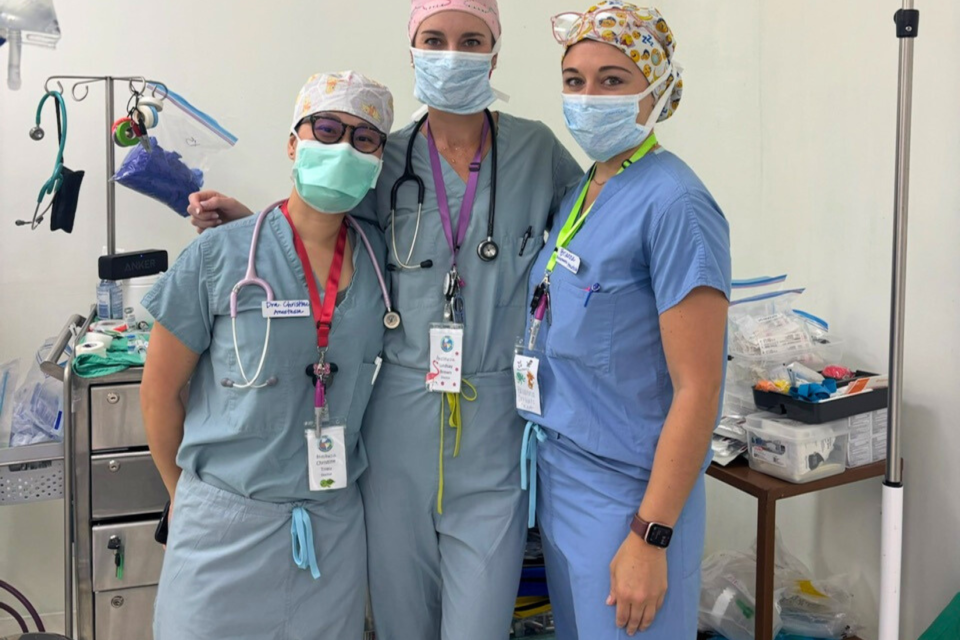 Three healthcare professionals in scrubs and masks posing together in a clinical setting.