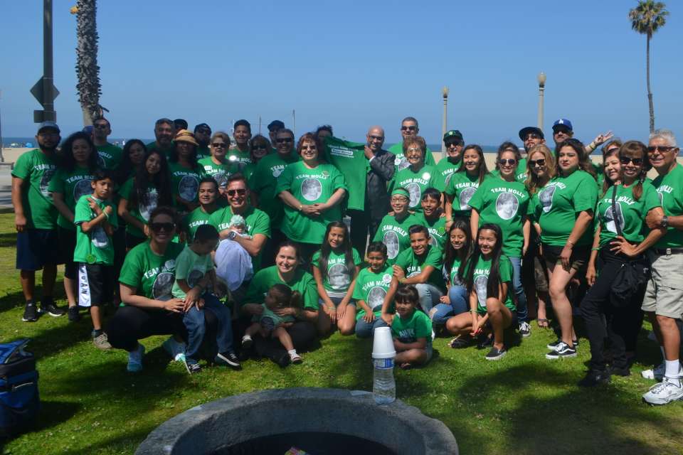 A large group of people wearing green shirts gather outdoors near the beach.
