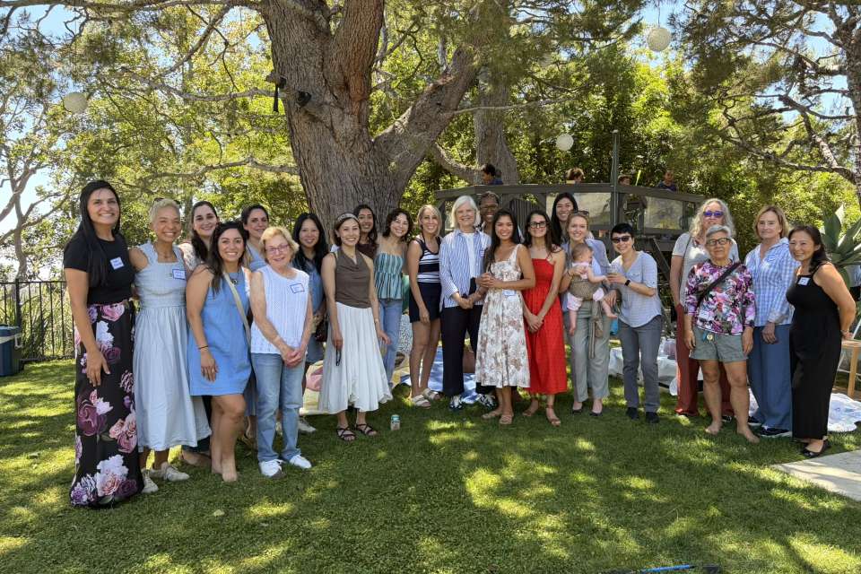 About 25 people posing together on a lawn beneath a large tree