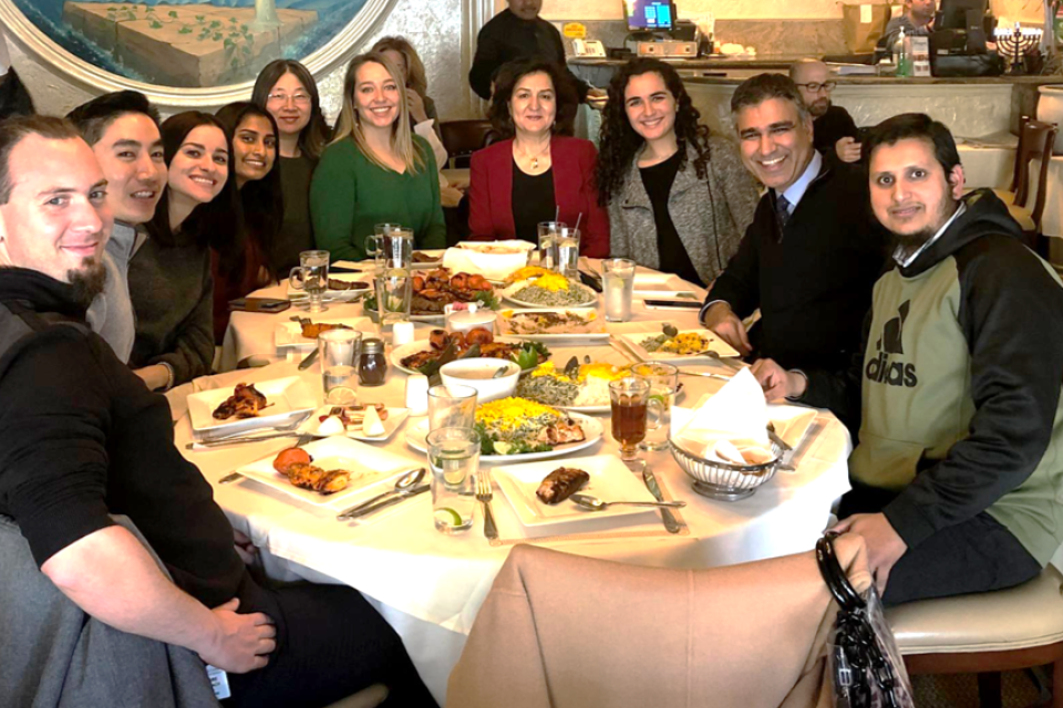  A diverse group of Eghbali lab team members are seated around a restaurant table laden with food and drinks, smiling for the camera.