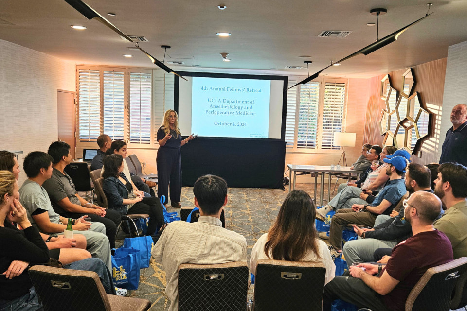 Maxime Cannesson, MD, PhD presents to a group in a workshop setting. The banner in the background indicates it's the "4th Annual Fellows' Retreat."
