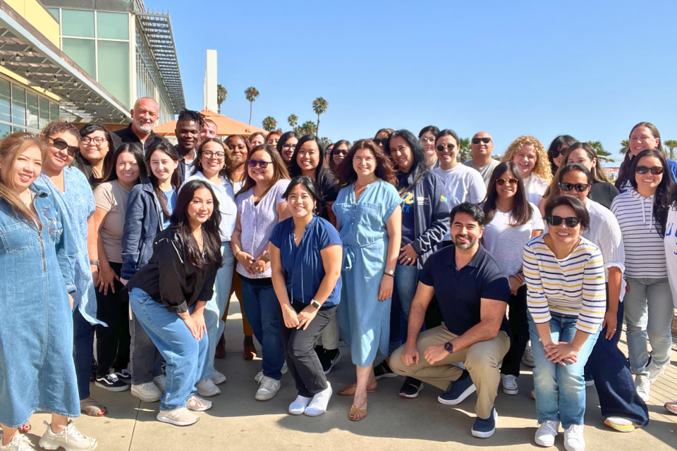 Group of Administration staff posing as group at the 2024 DAPM Annual Retreat with palm trees visible in the background.