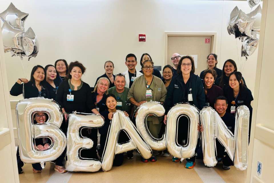 A group of medical professionals in a hospital setting with silver balloons spelling "BEACON"
