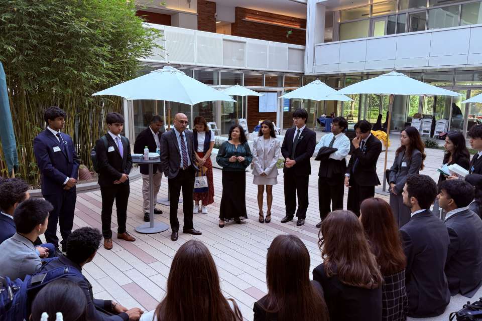 Group of people in formal attire gathered outdoors, engaged in a discussion.