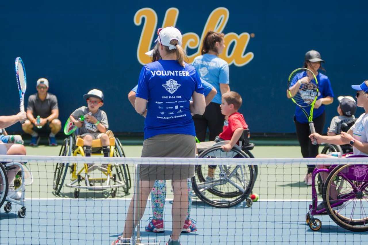 a group of children in wheelchairs playing games in an outdoor UCLA tennis court