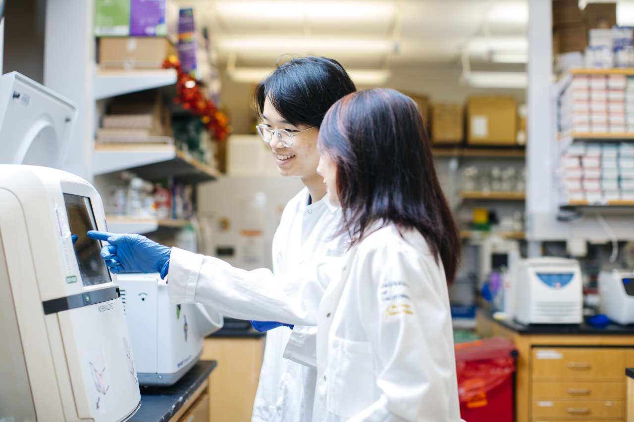 Two scientists in white coats using a lab analyzer.