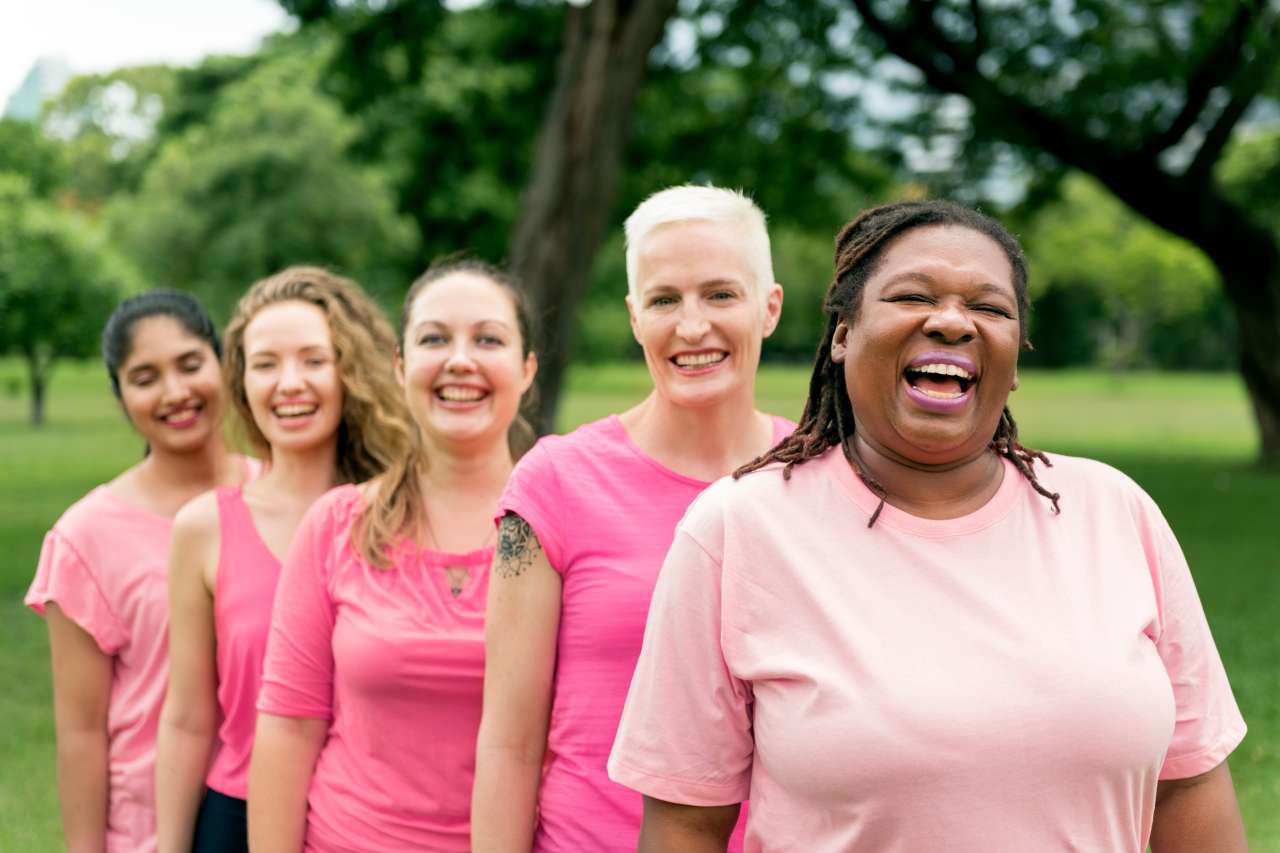 Five women in pink shirts standing together smiling