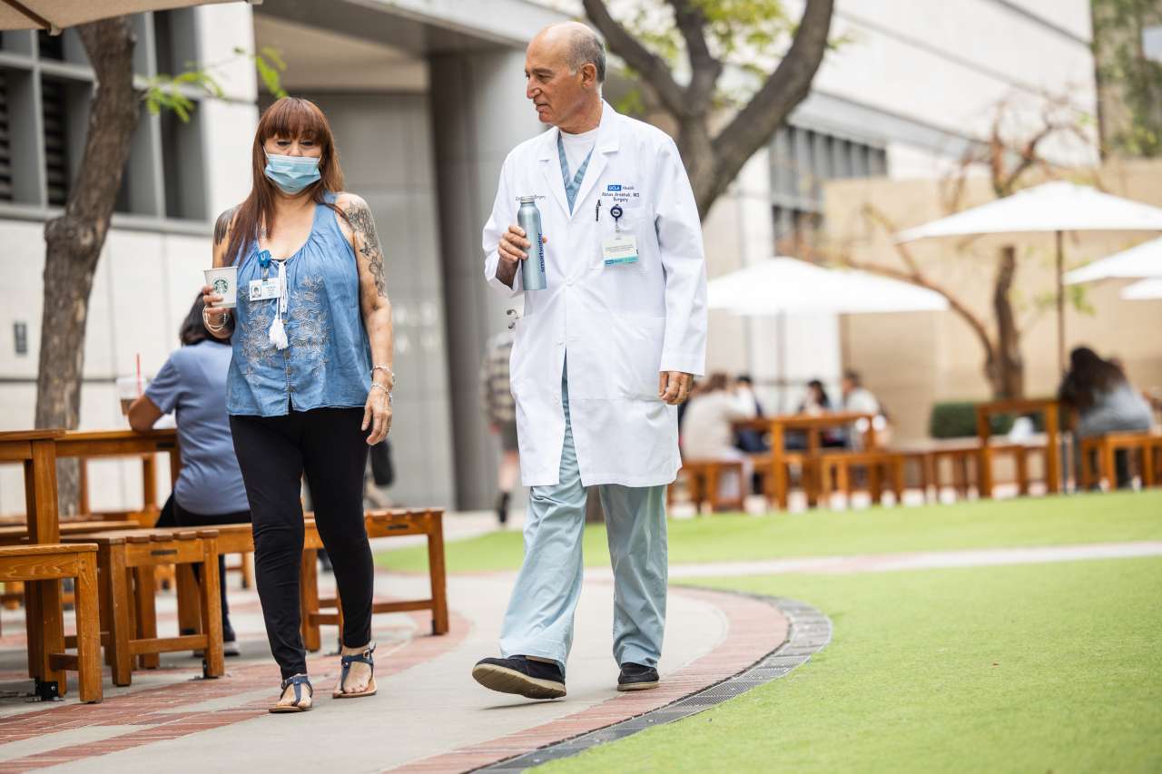 A doctor and patient walk through a hospital courtyard.