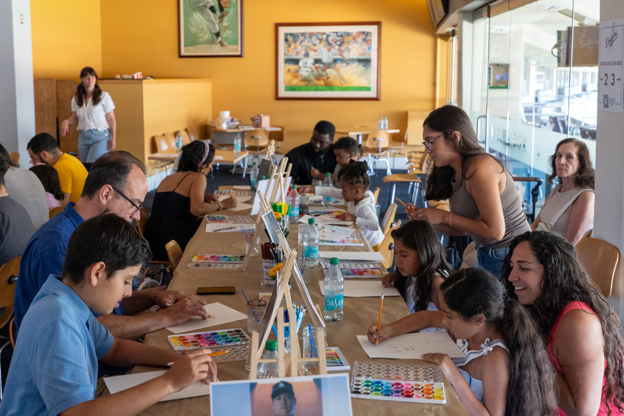 Pediatric cancer patients sit at a long table drawing sketches of Dodgers players during an art workshop.