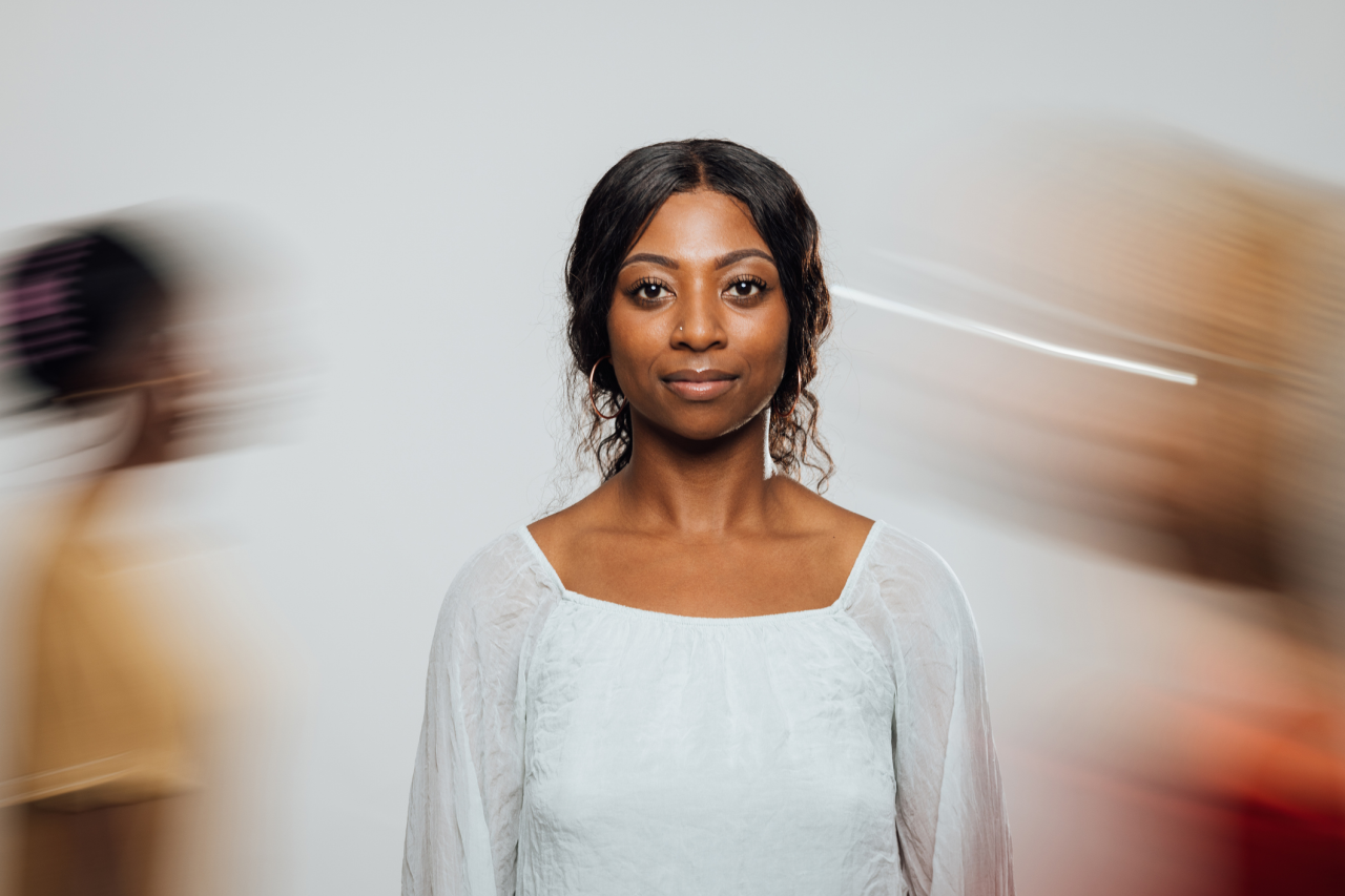 A woman looking at the camera with two people blurred in motion behind her