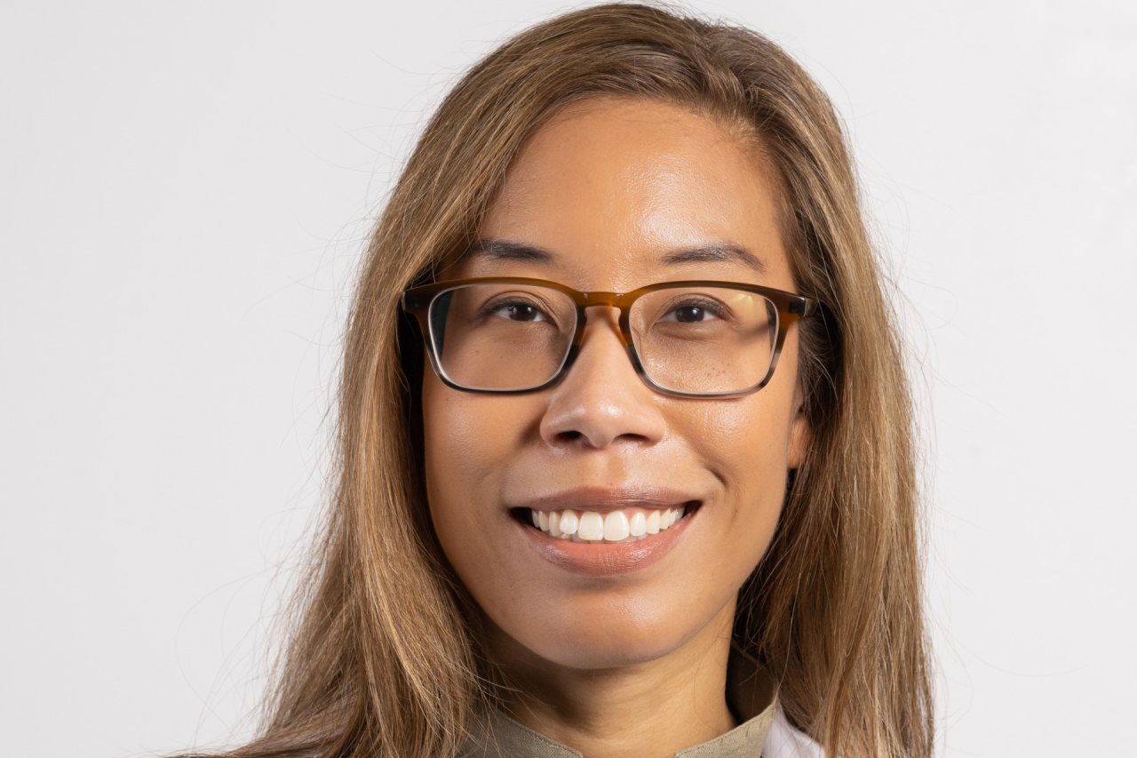 A medical professional wearing a lab coat with a neutral background.