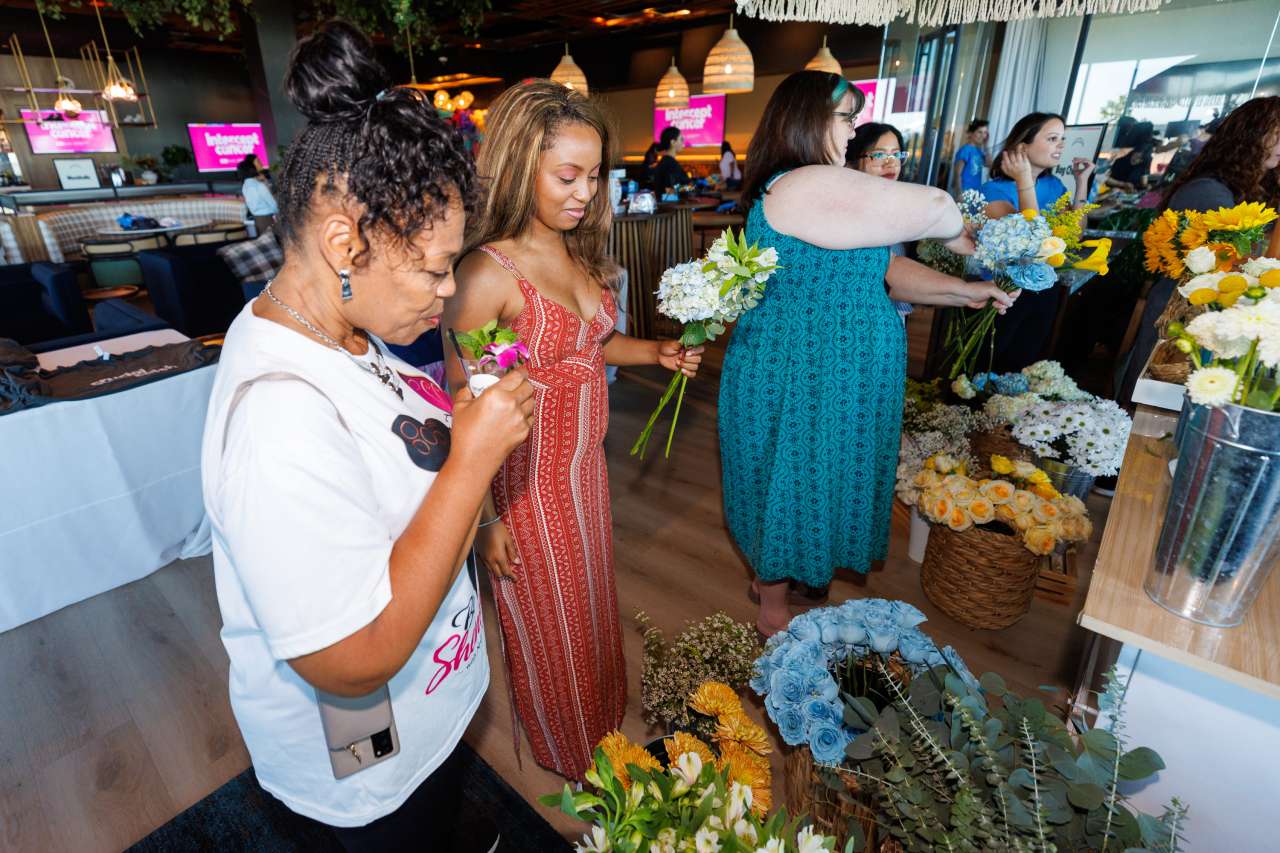 Two women hold flowers at a make-your-own bouquet table. 