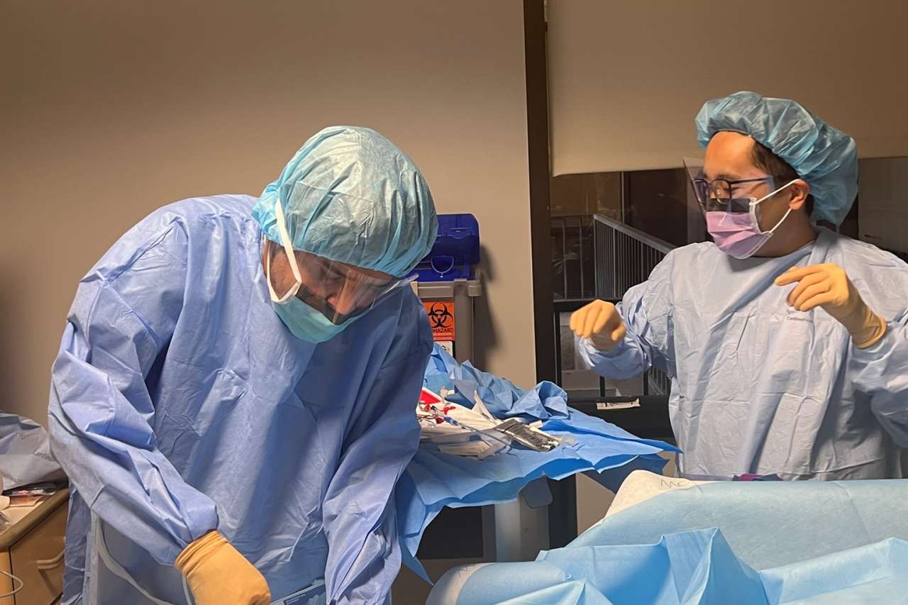 Two masked pulmonary fellows in blue gowns operating over a draped patient