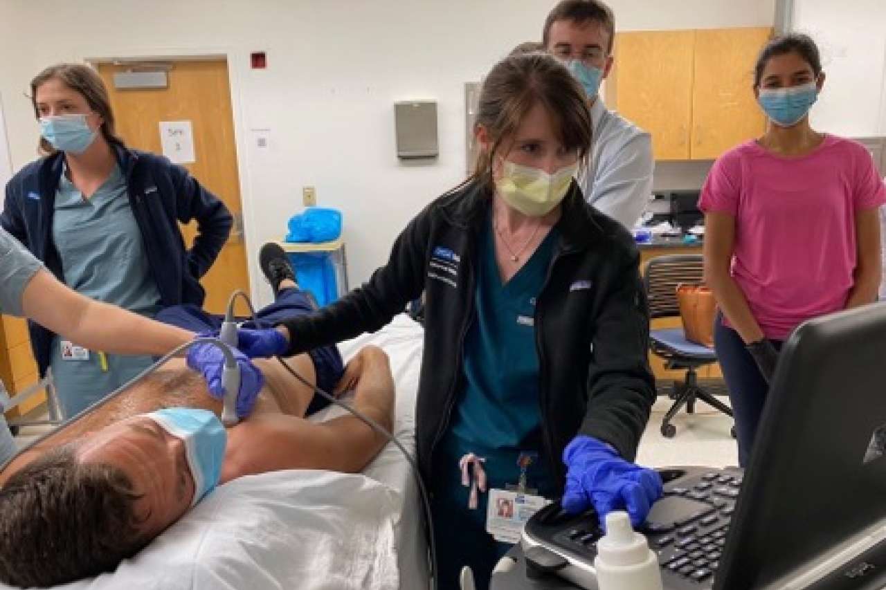 A doctor conducting a training on a volunteer with the ultra-sound equipment while other physicians watch