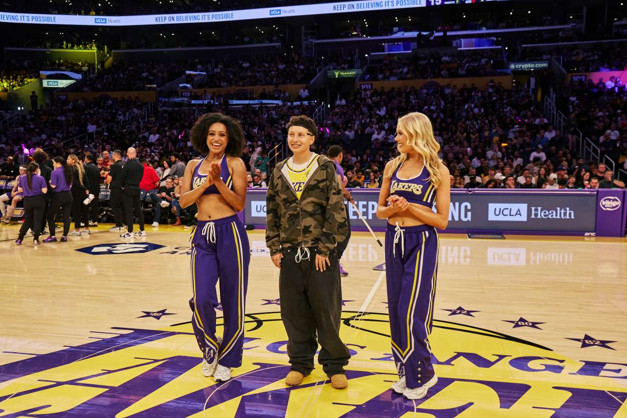 A teen girl stands with two Los Angeles Lakers cheerleaders on the basketball court.