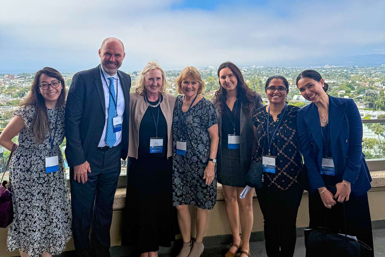 Group of six people in formal attire posing outdoors with a city view in the background.
