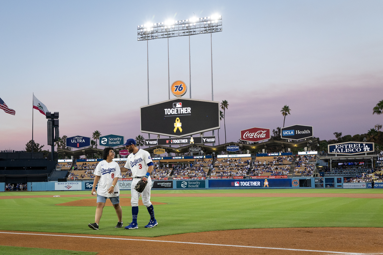 UCLA Health pediatric cancer patient Angela Unayan walks off the field with Dodgers outfielder Chris Taylor after throwing out the ceremonial first pitch.