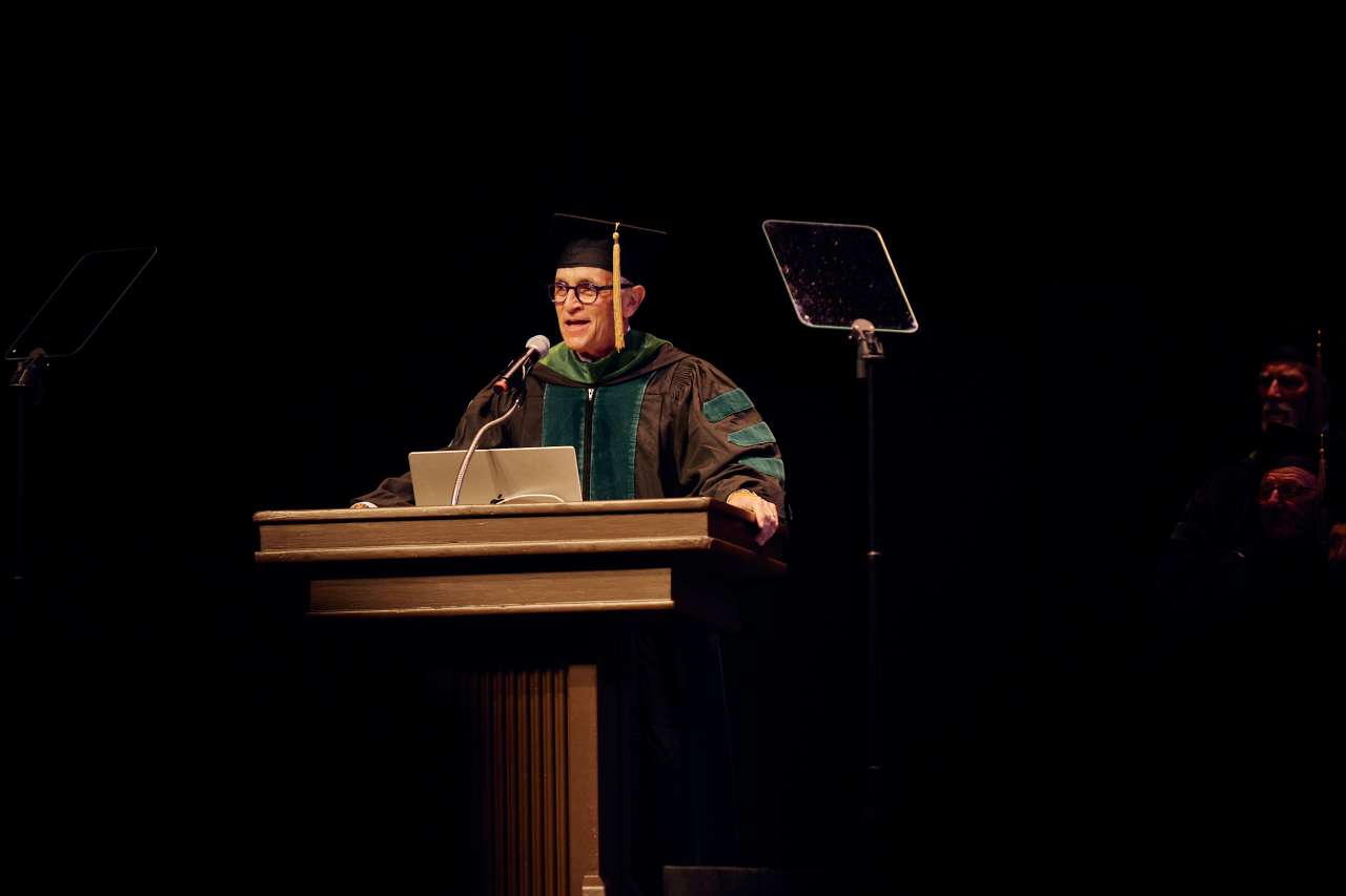 UCLA medical school commencement speaker, Dr. Joe Sachs, speaks at a podium during the graduation ceremony.