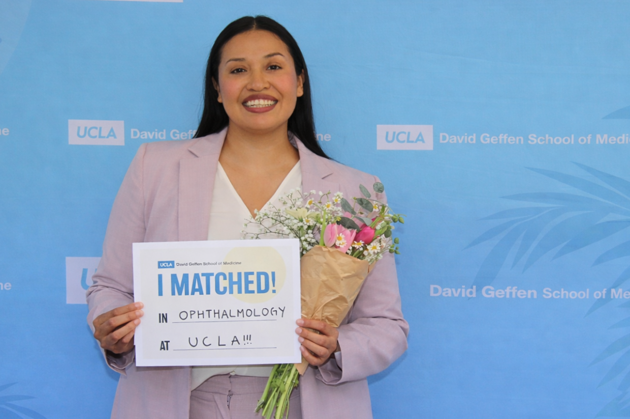 UCLA medical student Karla Murillo holds her Match Day card in front of a UCLA-themed backdrop.
