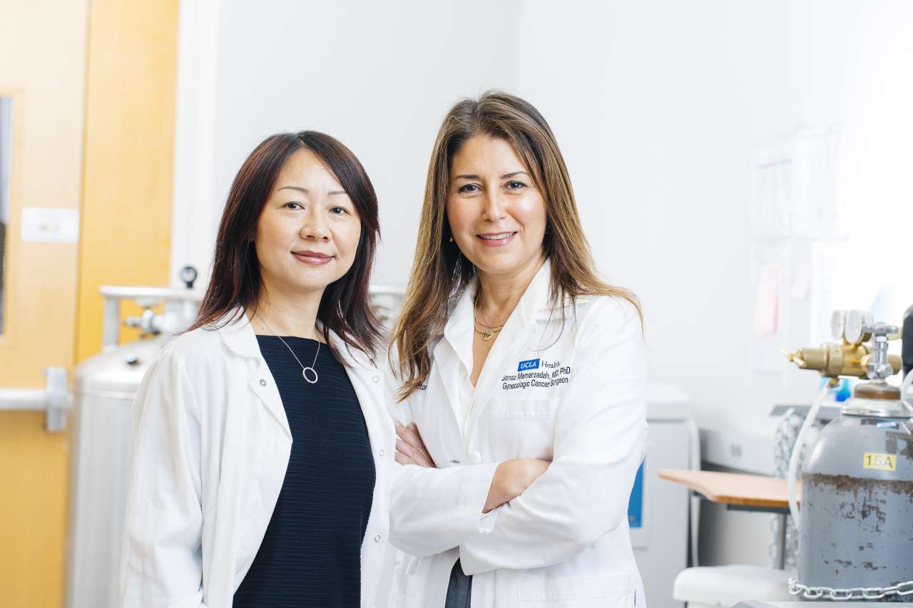 Dr. Lili Yang (left) and Dr. Sanaz Memarzadeh (right) both wearing white lab coats inside a research lab