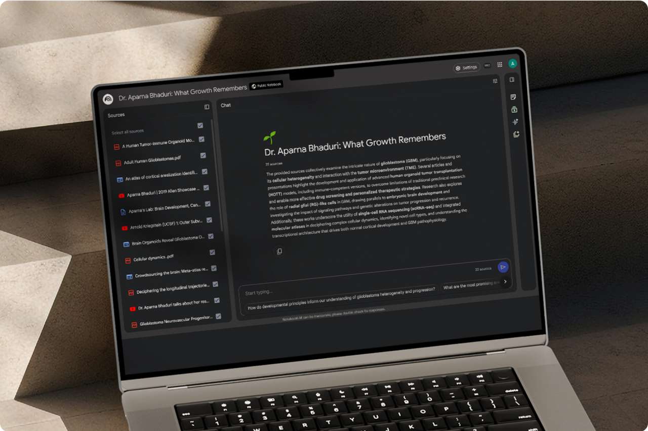 A high-angle view of a gray laptop in a dark, minimalist setting. The screen shows a Google Gemini interface with a block of text.