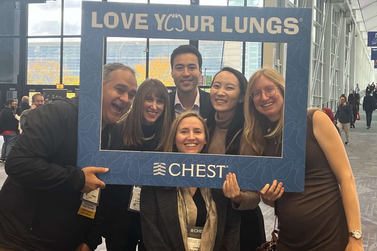 Five people smiling, holding a "LOVE YOUR LUNGS" CHEST frame at a convention hall