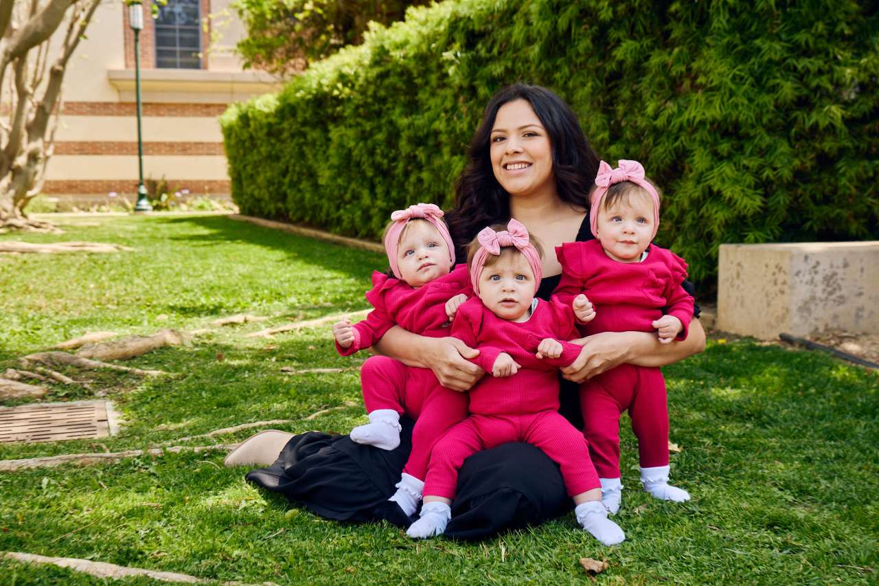 A mom sits with her identical triplet girls.