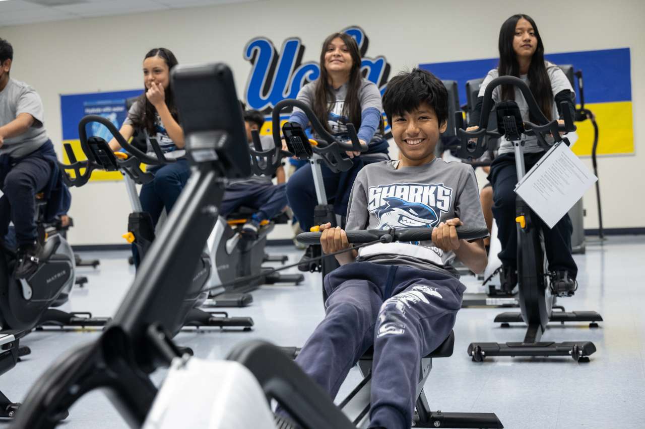 A group of kids at an adaptive gym, smiling and using exercise bikes and rowing machines