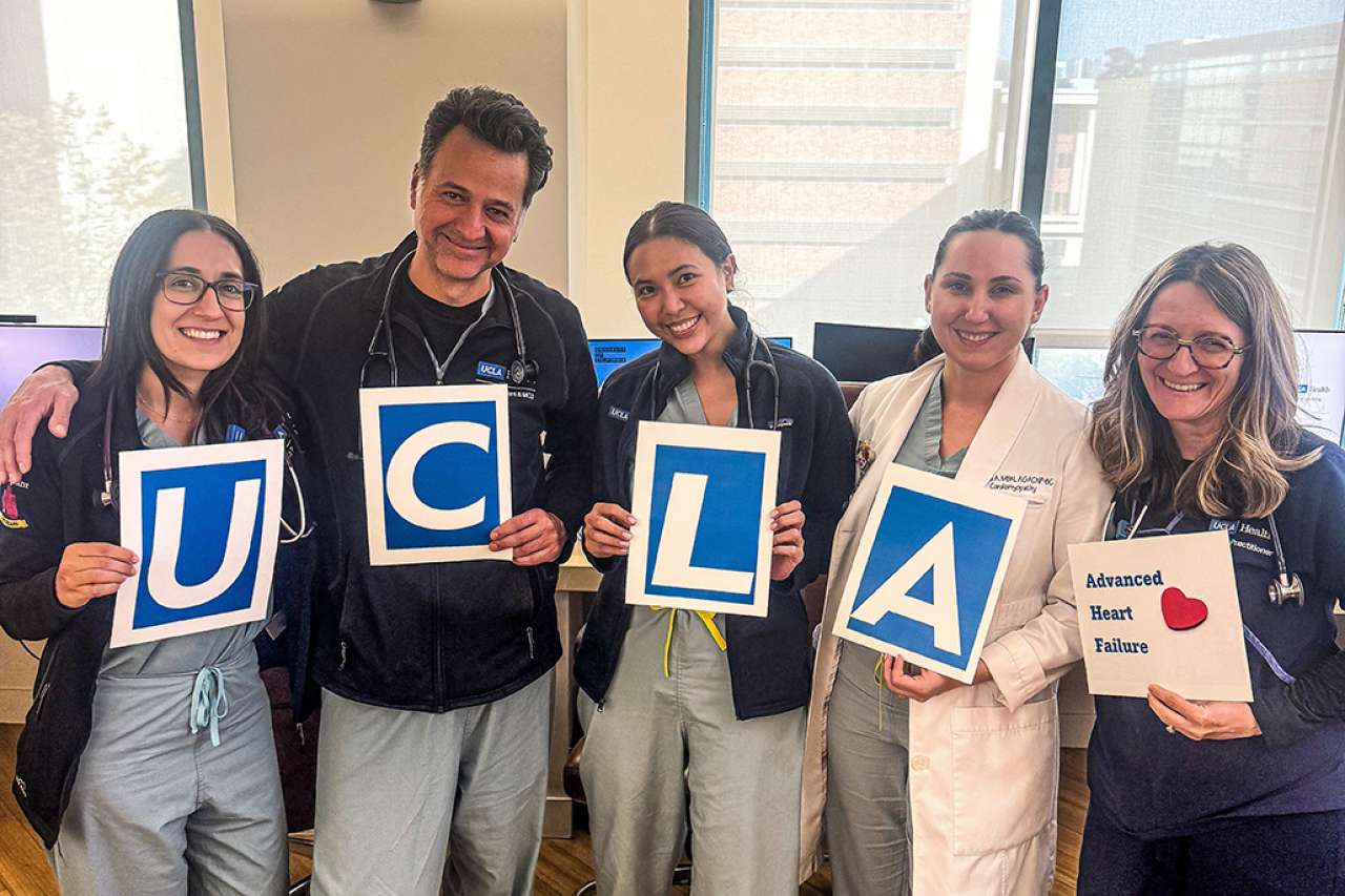 Five medical professionals hold signs spelling "UCLA" in a well-lit office space.