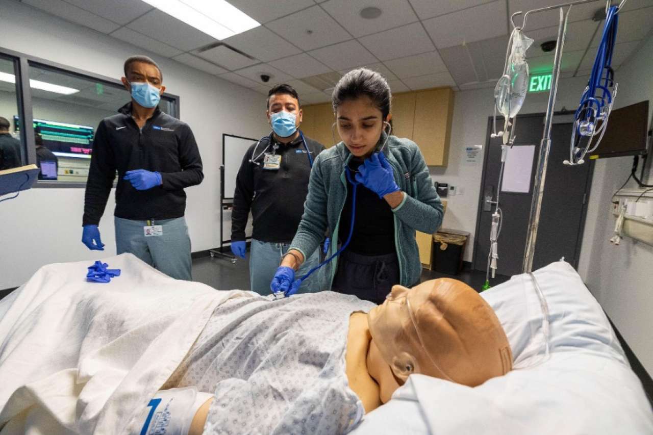 a dummy patient in a bed with a doctor standing over with a stethascope and other around