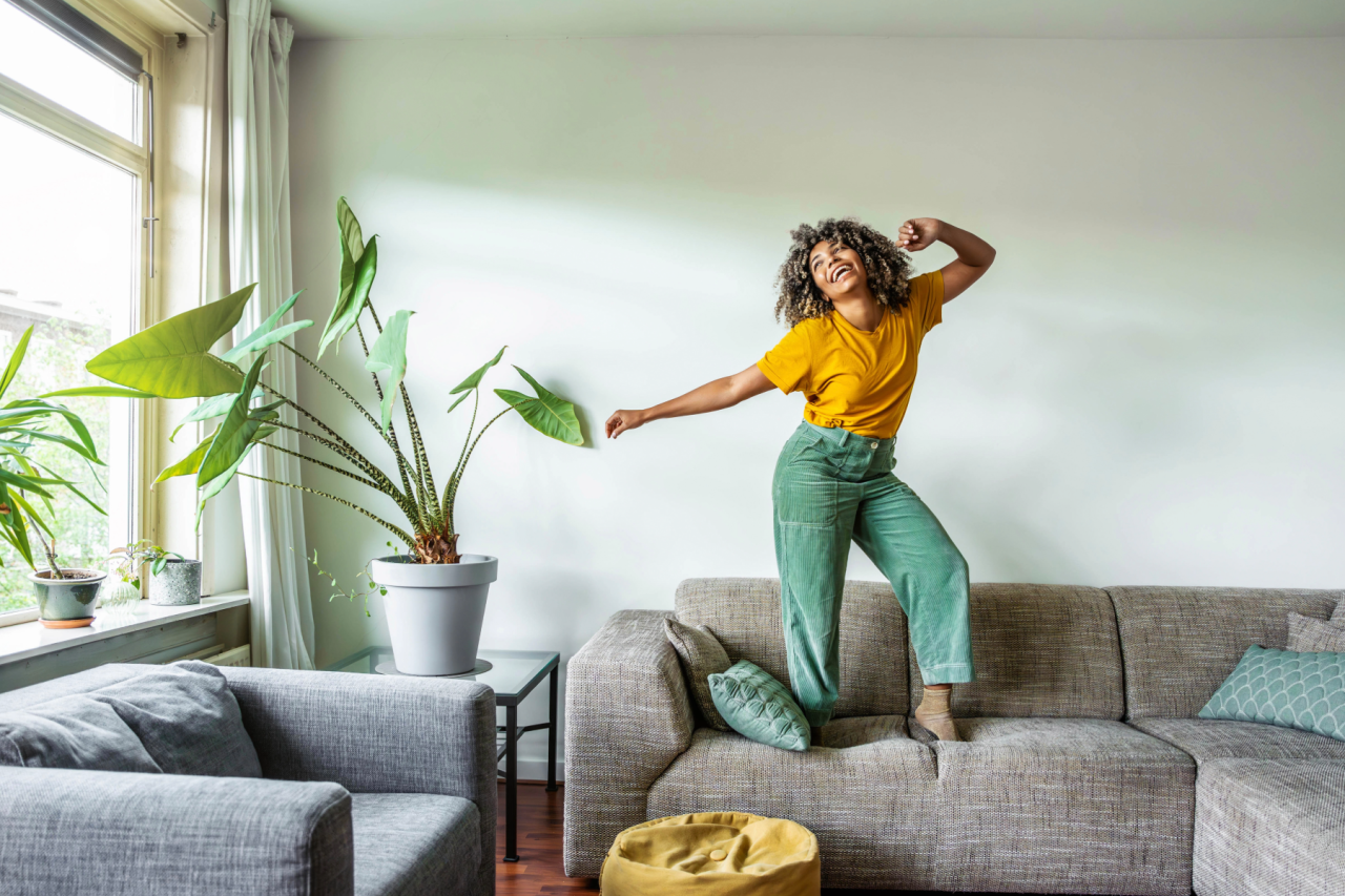 Person dancing on living room couch next to large potted plants