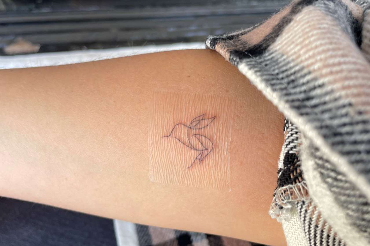 A hummingbird tattoo is shown a woman's arm.