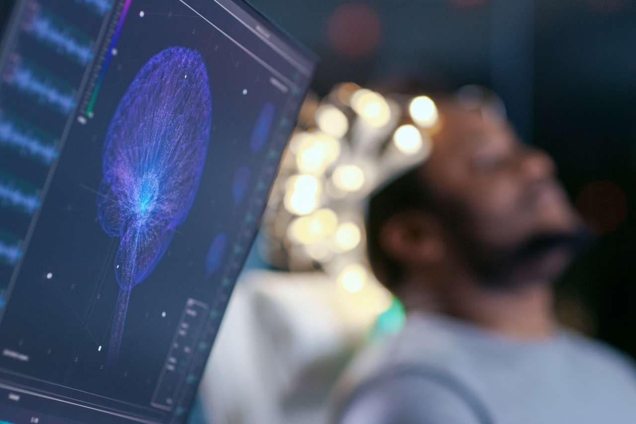 Man wearing EEG cap beside monitor displaying brain activity scan