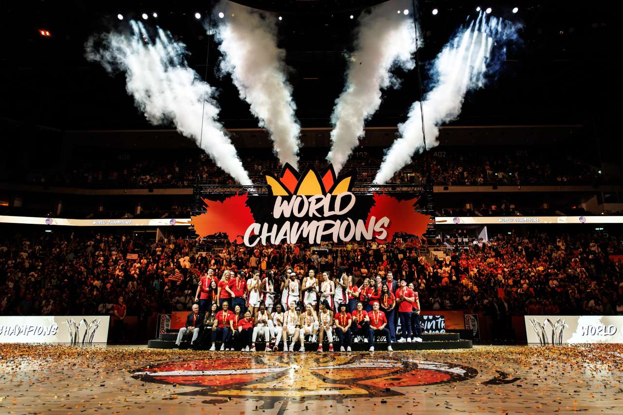 A team poses on a basketball court in front of a World Champions sign.