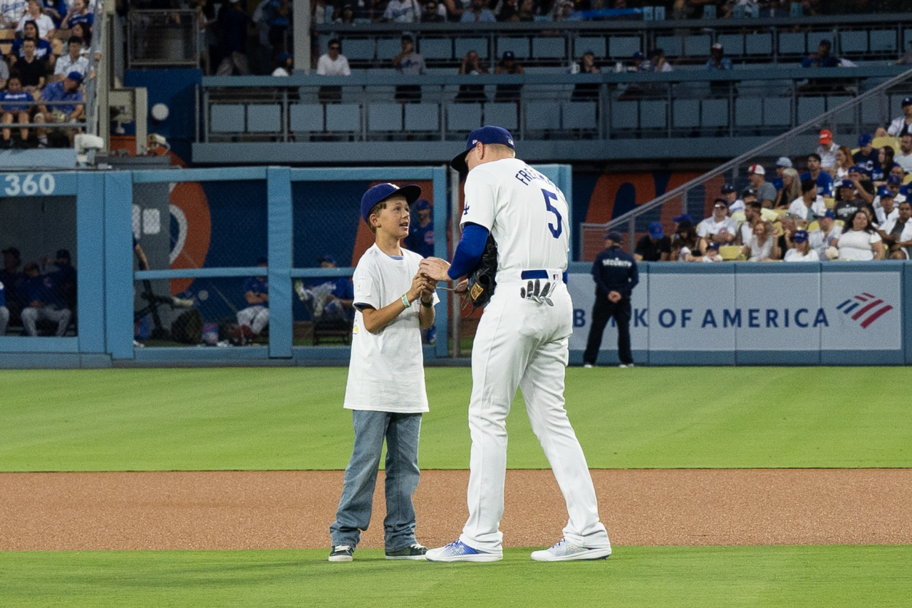 Dodgers first baseman Freddie Freeman, wearing number 5, is autographing a baseball for a young fan, Bodhi Bennett, on the field.