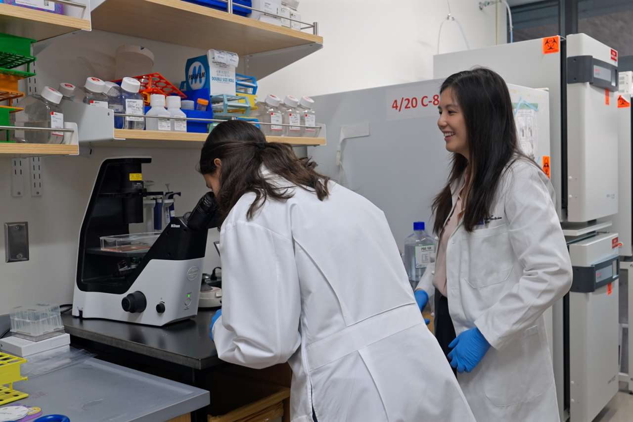 Two researchers in lab coats operating equipment at a laboratory bench.