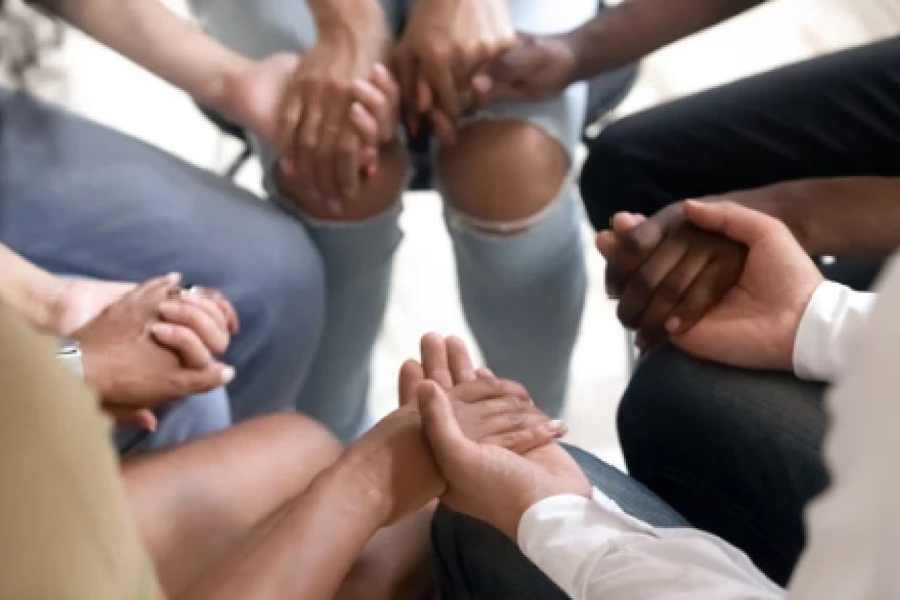 5 people sitting in a circle holding hands in support.