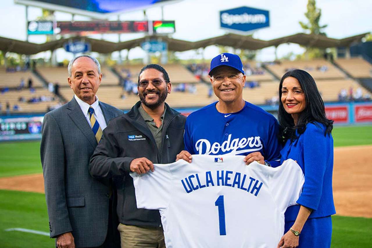 UCLA Health leaders and Dodgers coach holding a uniform with the writing that says UCLA Health 1.