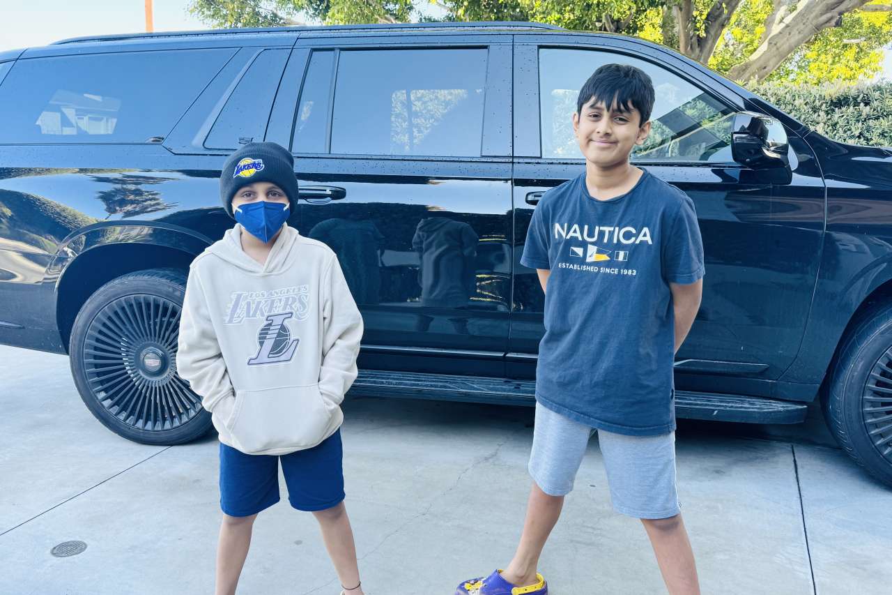 Two brothers stand next to each other in front of an SUV.