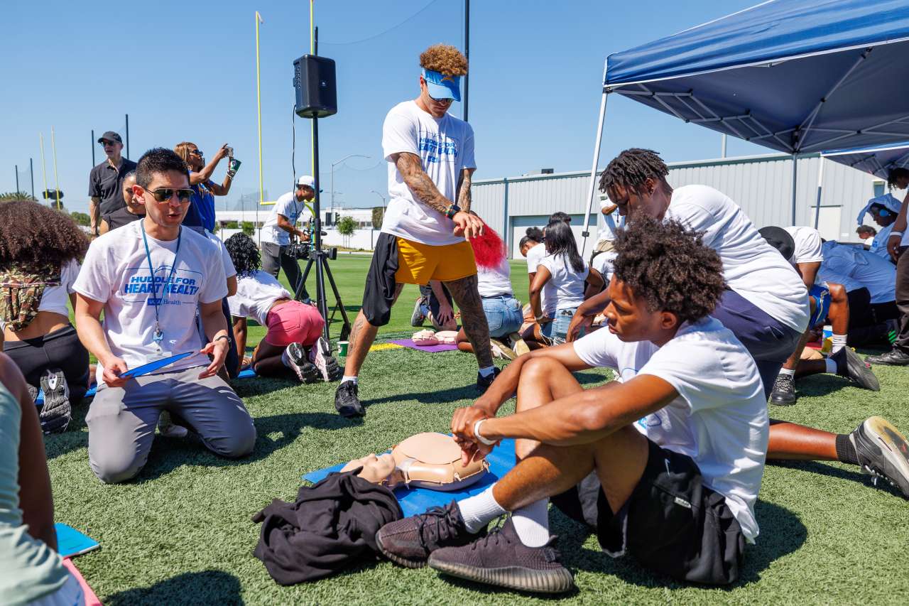 A football player helps high schoolers learn CPR skills.