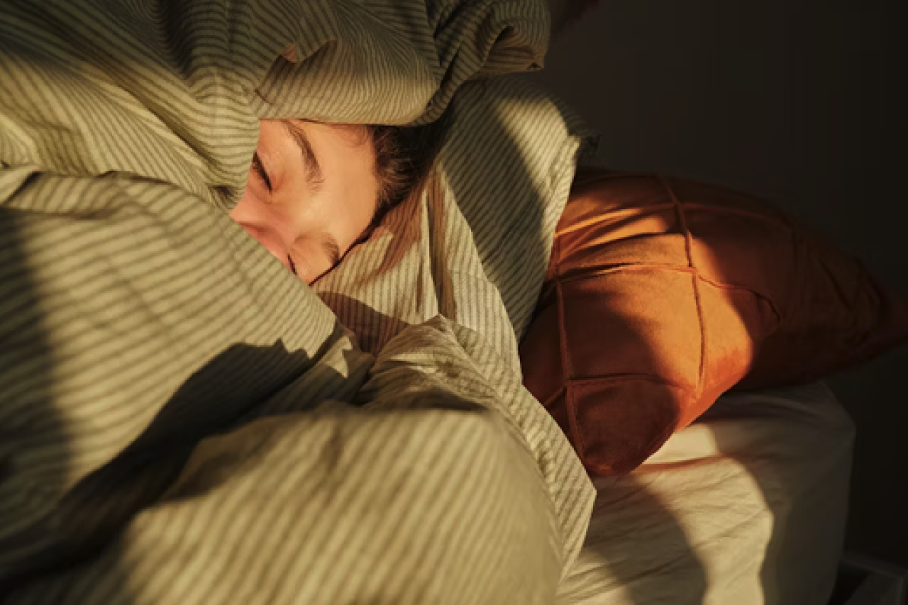 A person in bed covering themselves in a gree bed sheet