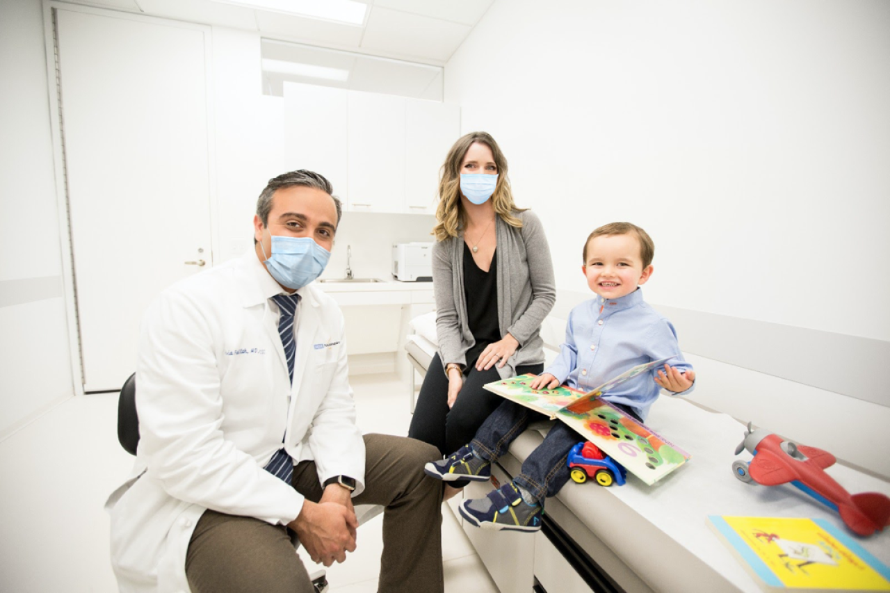 Doctor and woman, wearing masks, at doctor's office visit with young son
