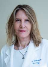 Woman wearing white medical coat facing camera, neutral background