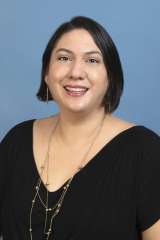 Karla Lagunas wearing a black v-neck shirt, smiling and looking at the camera in a professional setting 