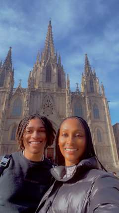Two people in coats taking a selfie in front of a cathedral under blue sky