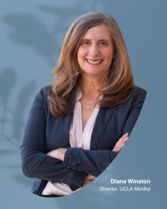 Diana Winston stands smiling with arms crossed against a blue background with leaf shadows. Text: ‘Diana Winston, Director, UCLA Mindful.