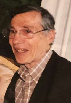 Leonard Walts with glasses smiles while wearing a plaid shirt and dark jacket.