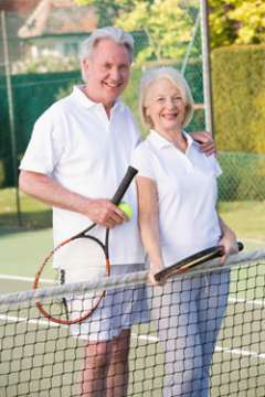 Older caucasian couple on the tennis court holding tennis rackets.