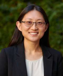 Headshot of Jiaying Gallati in a dark blazer with green foliage background.